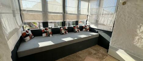 A cozy reading nook with a cushioned bench, large windows, and a view of the outdoors.