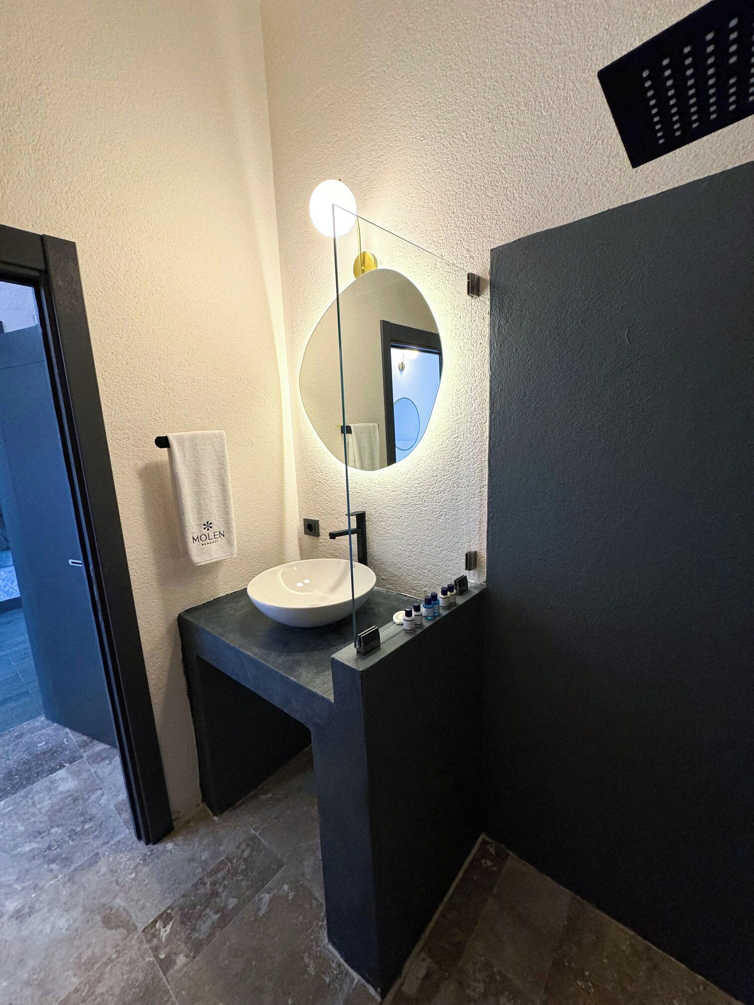 Een moderne badkamer met een ronde spiegel, een witte wastafel en een handdoek aan een haak.