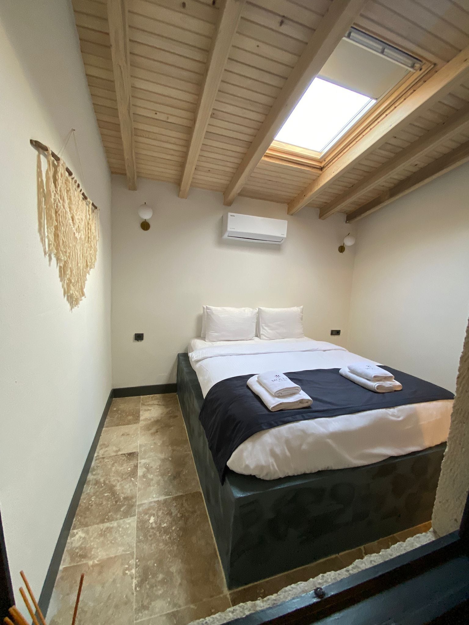 Une chambre à coucher avec un lit, des murs blancs, une lucarne et un appareil de climatisation.