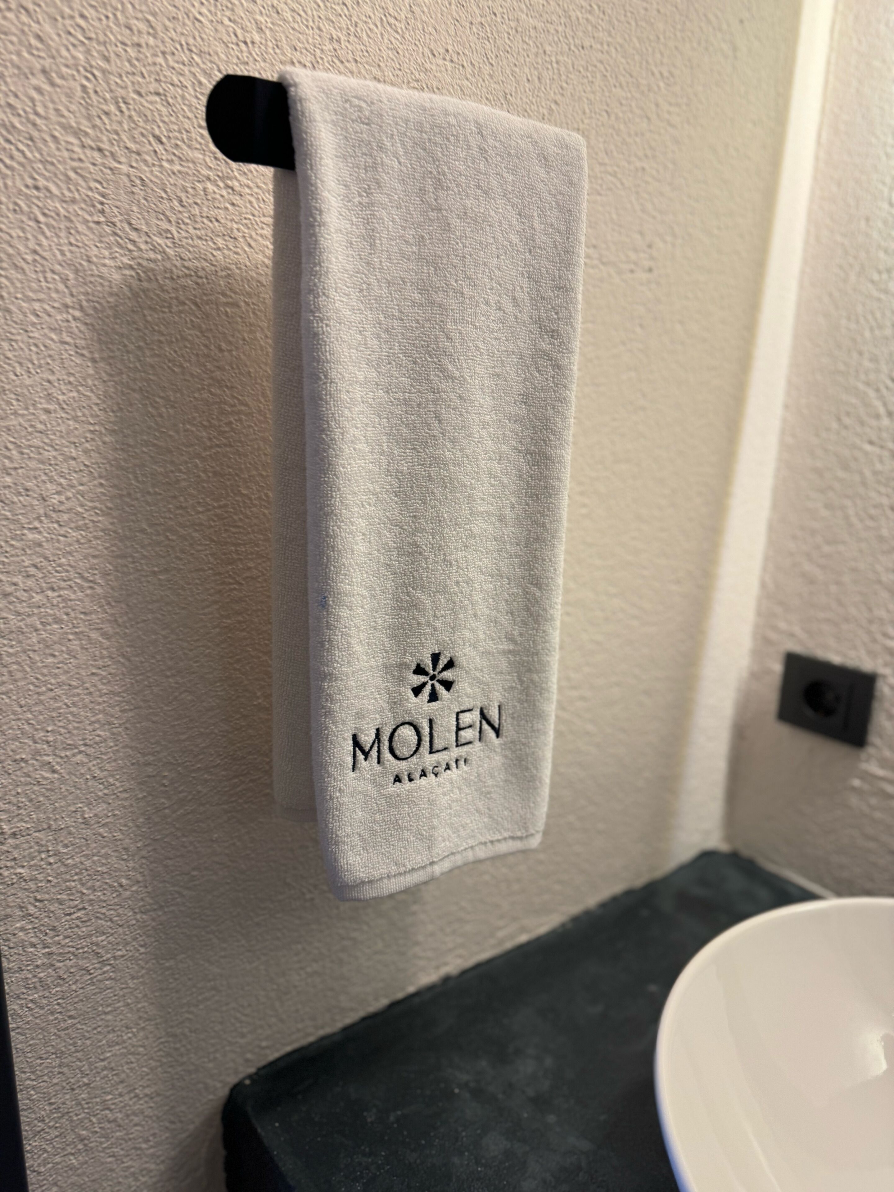 Una toalla colgada en un gancho con el logo "MOLEN" y el texto "AEÇAT".