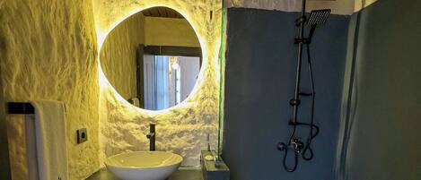 A bathroom with a stone sink, a round mirror, and a shower.