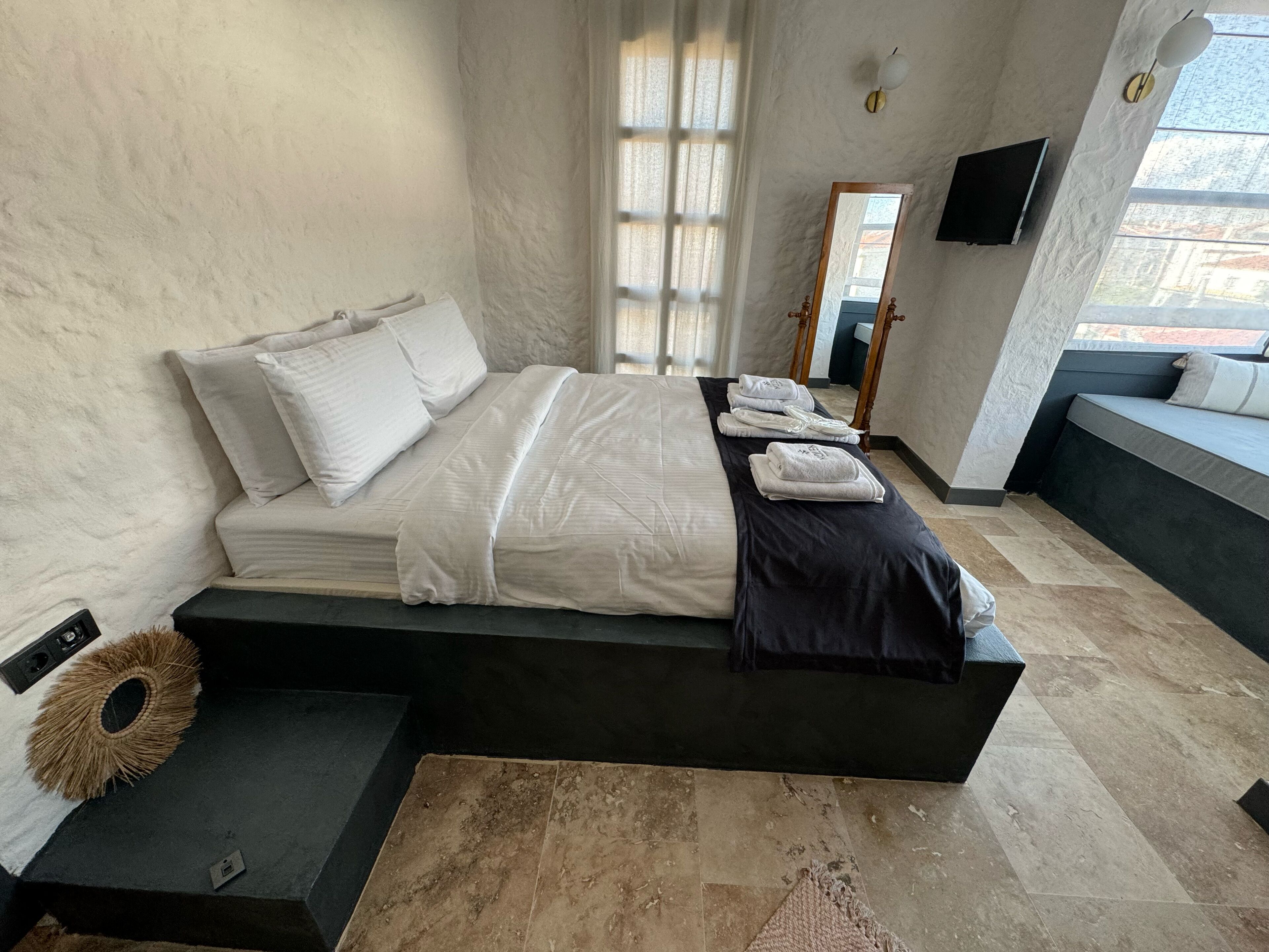 A modern bedroom with a bed, bedside tables, a mirror, and a view of the outside.