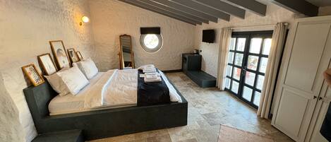 A bedroom with a large bed, a bedside table, a mirror, a small seating area, and a wardrobe.