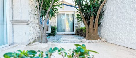 A narrow pathway leading to a building with a stone facade and a glass door.