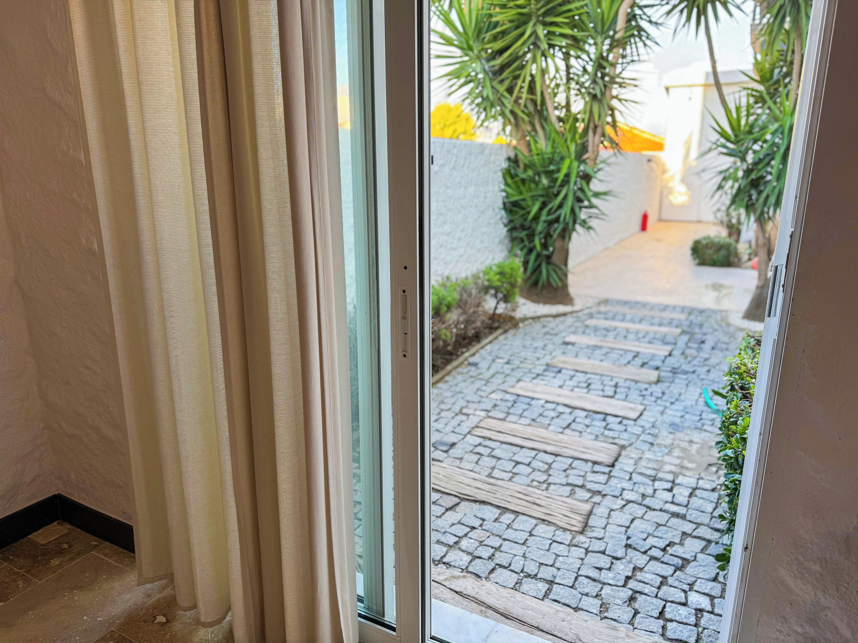 A doorway with a view of a cobblestone path leading to a garden area with plants and a yellow structure.