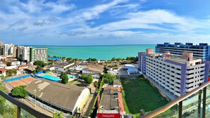 A coastal cityscape with a view of the sea, high-rise buildings, and a large hotel with a swimming pool. - Edf. Gales de Pajuçara - Apt. 105 (Pajuçara Maceió)