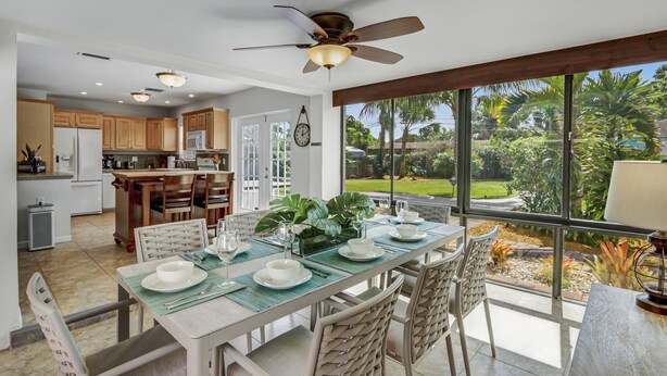 A spacious kitchen with wooden cabinets, a dining area with a table set for four, and a large window offering a view of a garden. - Work & Play Retreat. Private Office. 1GB Internet (Oakland Park)
