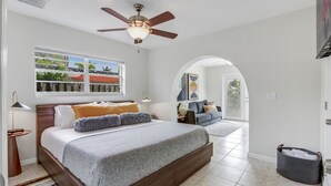 A bedroom with a large bed, a ceiling fan, a window with a view, and a door leading to another room. - Work & Play Retreat. Private Office. 1GB Internet (Oakland Park)