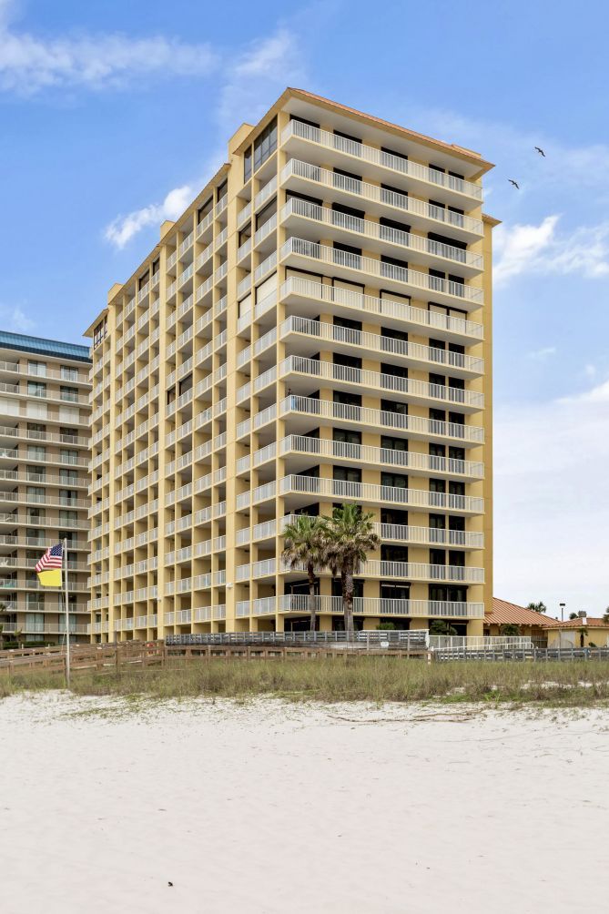 A multi-story hotel with balconies, located near a beach.