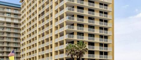 A multi-story hotel with balconies, located near a beach.