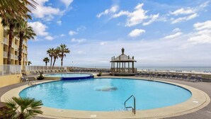 Una piscina circular con un pabellón, palmeras y vista al mar.