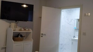 A bathroom with a television mounted above a sink, a white door, and a marble-tiled wall. - Citybreaks Rooms (Liverpool)