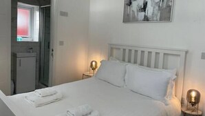 A hotel room with a bed, a bedside table with a lamp, a wall-mounted abstract painting, and a window with a red frame. - Citybreaks Rooms (Liverpool)