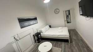 A bedroom with a bed, a bedside table, a lamp, a clock, a TV, and a radiator. - Citybreaks Rooms (Liverpool)