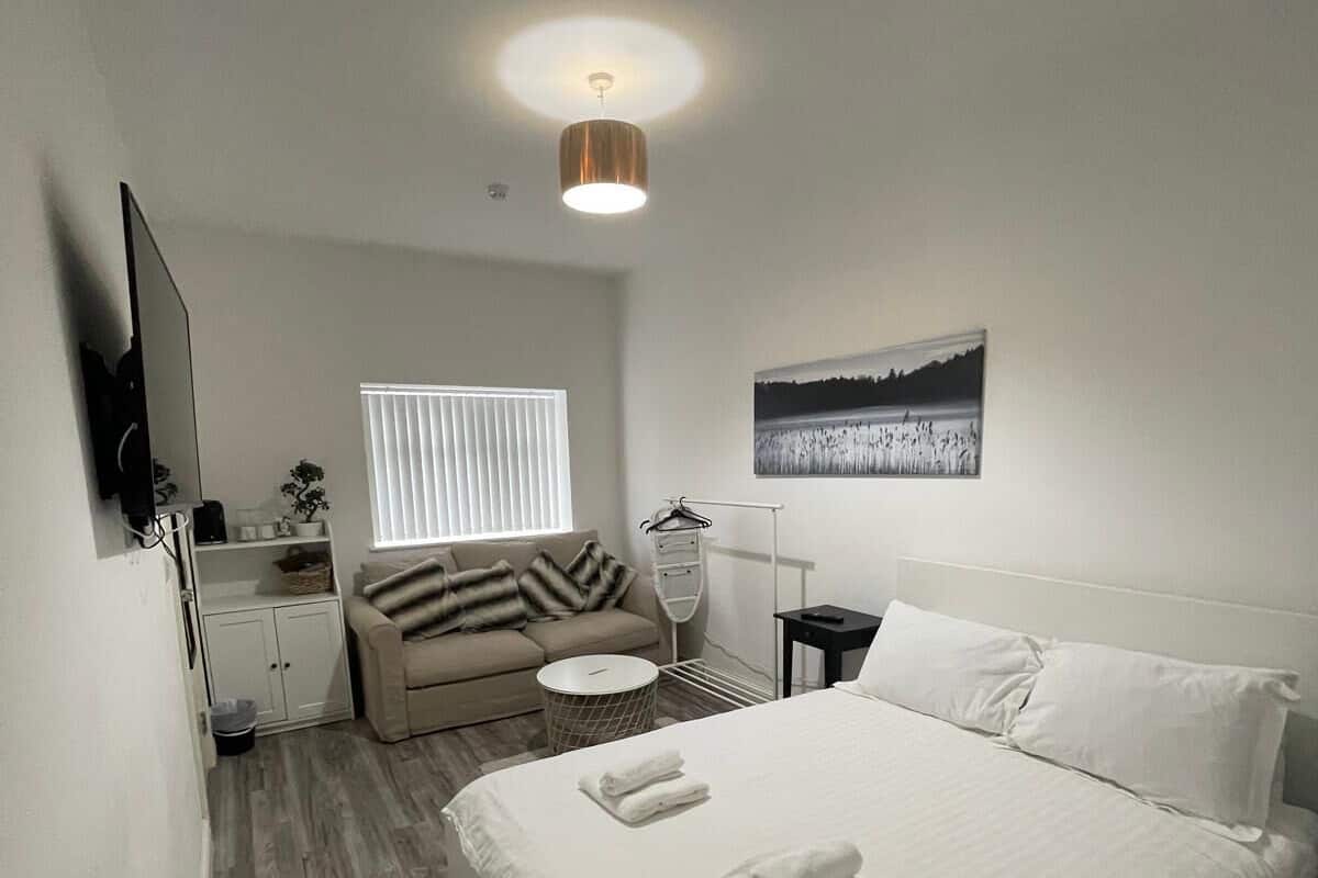 A modern bedroom with a large bed, a sofa, a TV, and a painting on the wall.