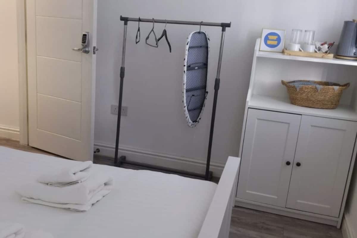 A hotel room with a bed, a wardrobe, a drying rack, and a small table with a basket.