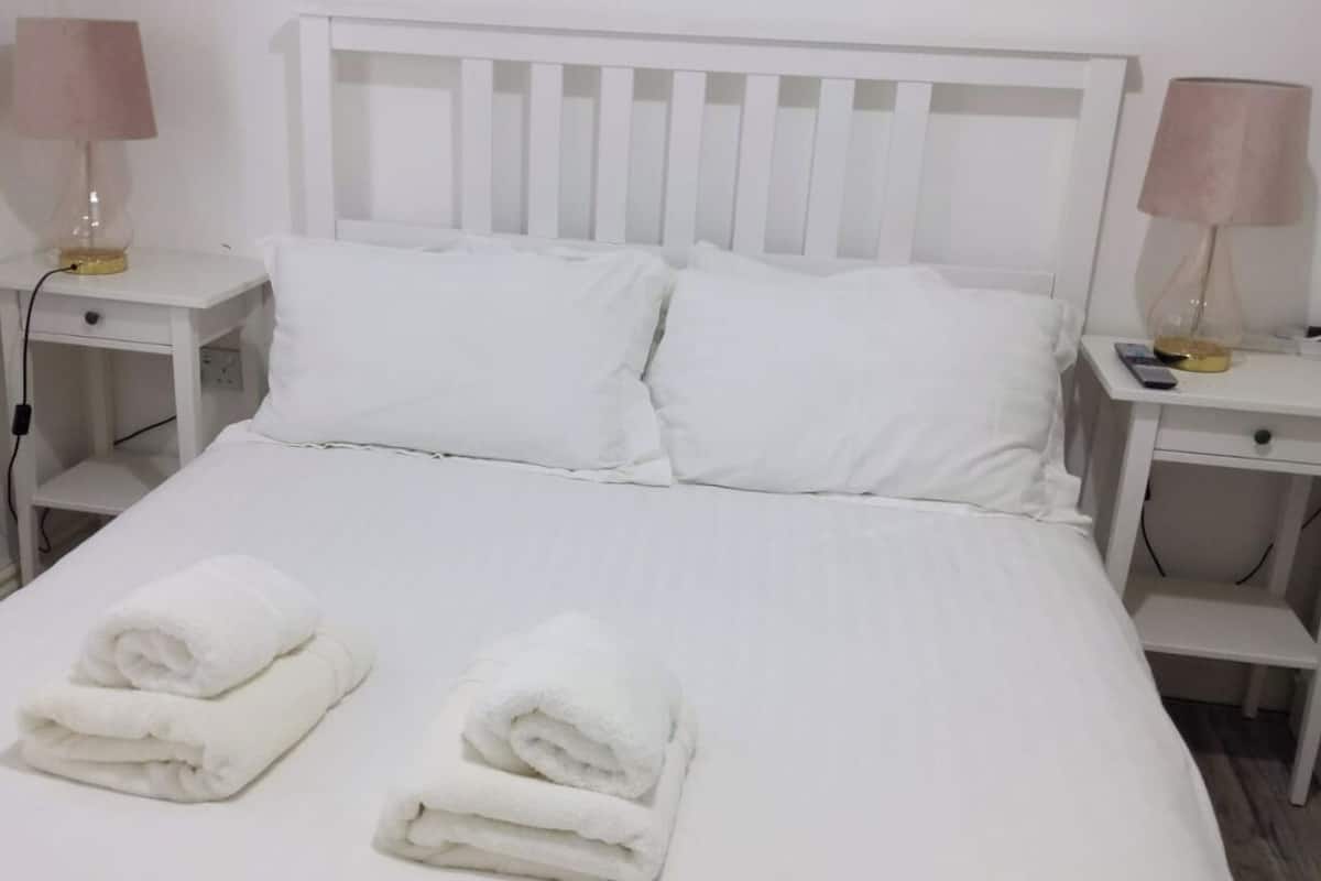 A neatly made bed with white bedding and pillows, two bedside tables with lamps, and folded towels on the bed.