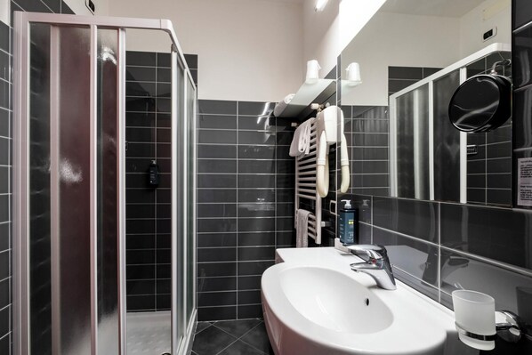 Un baño moderno con ducha de vidrio, lavamanos blanco y un espejo grande.