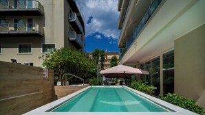 An outdoor swimming pool with a wooden fence, a patio area, and a view of adjacent buildings. - Cristallo Rimini (Rimini)