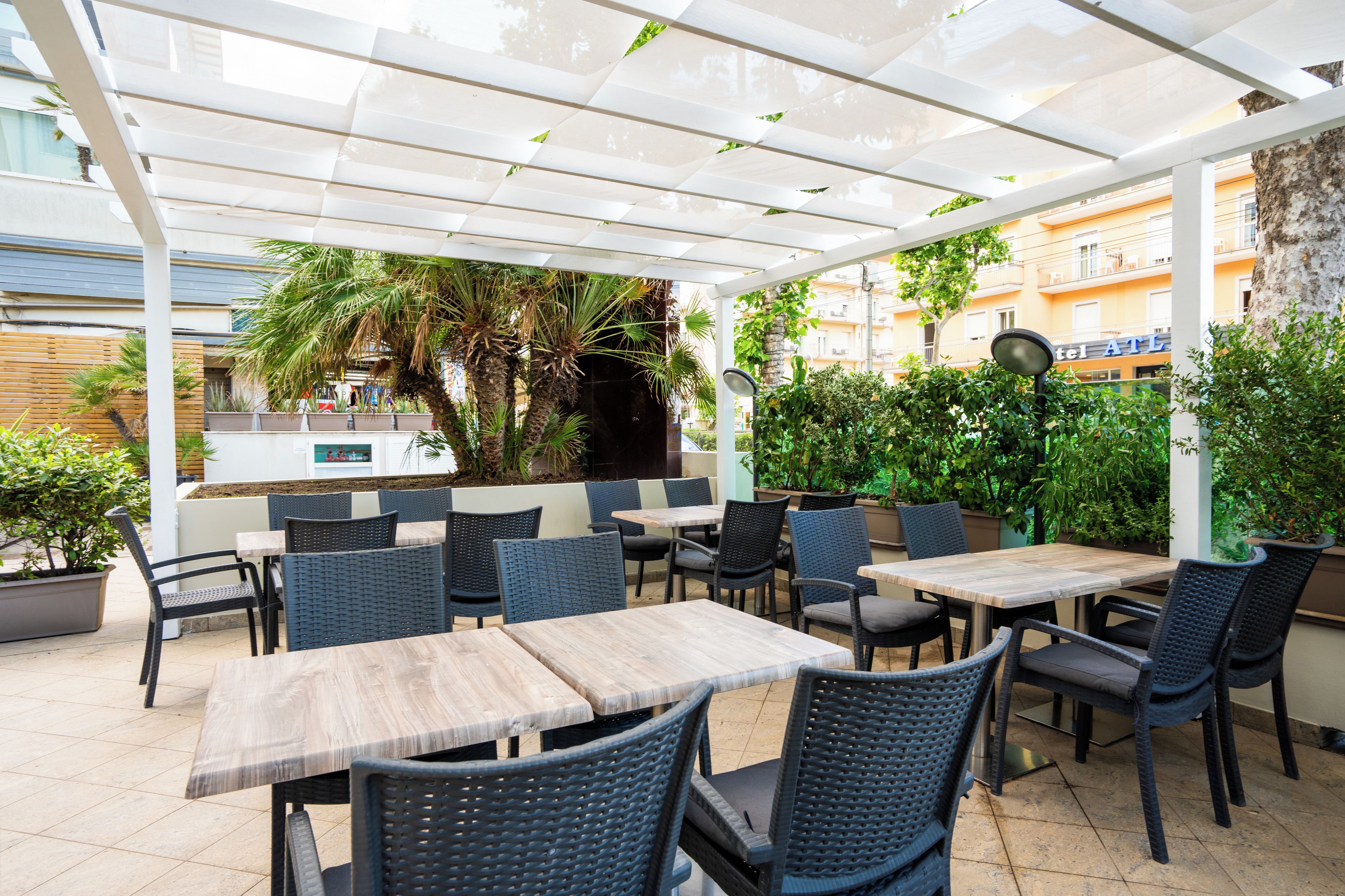 An outdoor patio area with tables and chairs, a white pergola, and potted plants.