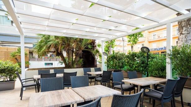 An outdoor patio area with tables and chairs, a white pergola, and potted plants.