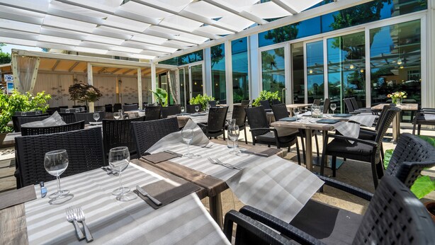 An outdoor dining area with tables and chairs, large windows, and a covered section. - Cristallo Rimini (Rimini)
