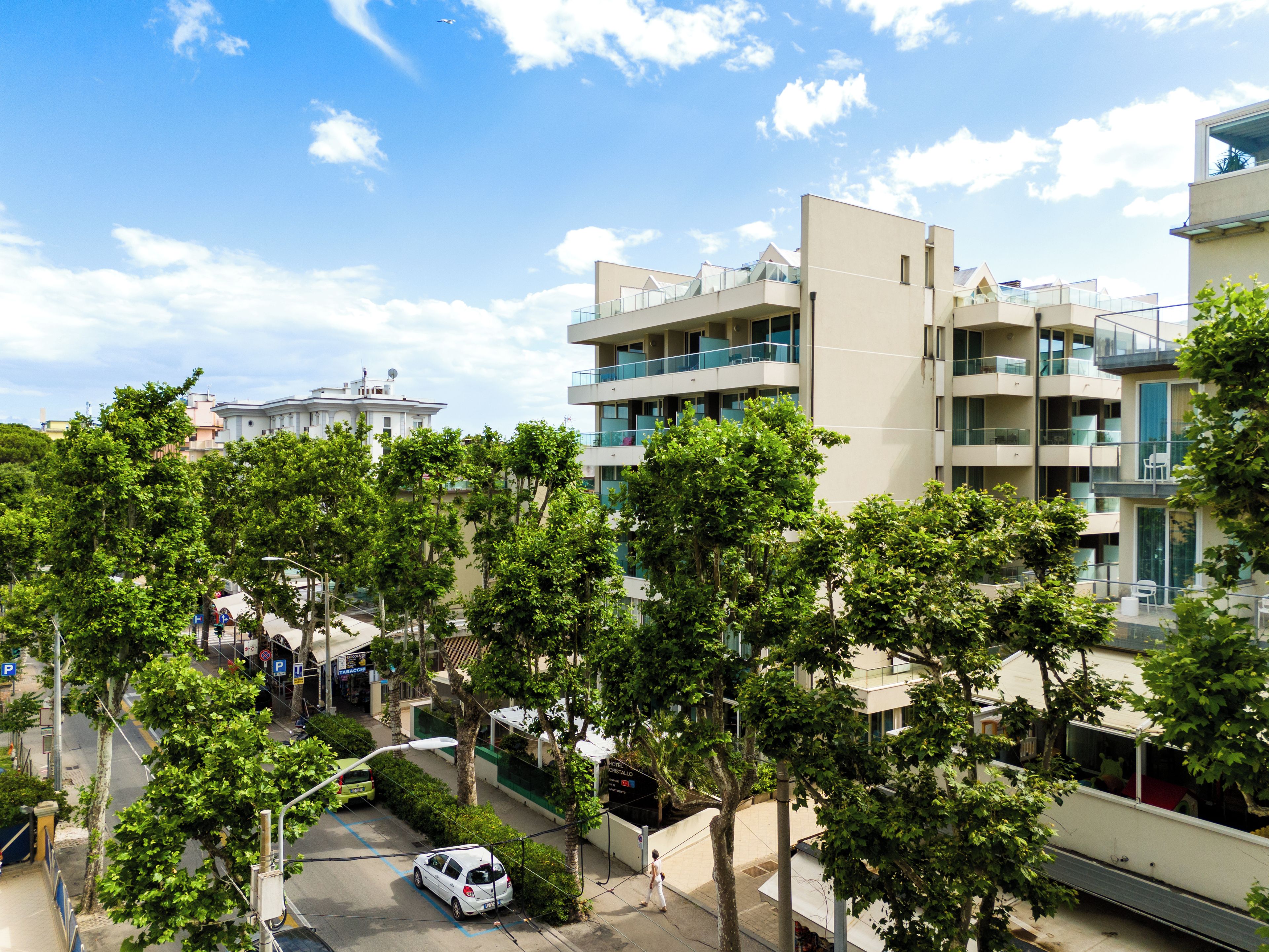 A modern building with multiple balconies, a clear sky, and surrounding greenery.