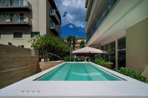 An outdoor swimming pool with a wooden fence, a patio area, and a view of adjacent buildings. - Cristallo Rimini (Rimini)