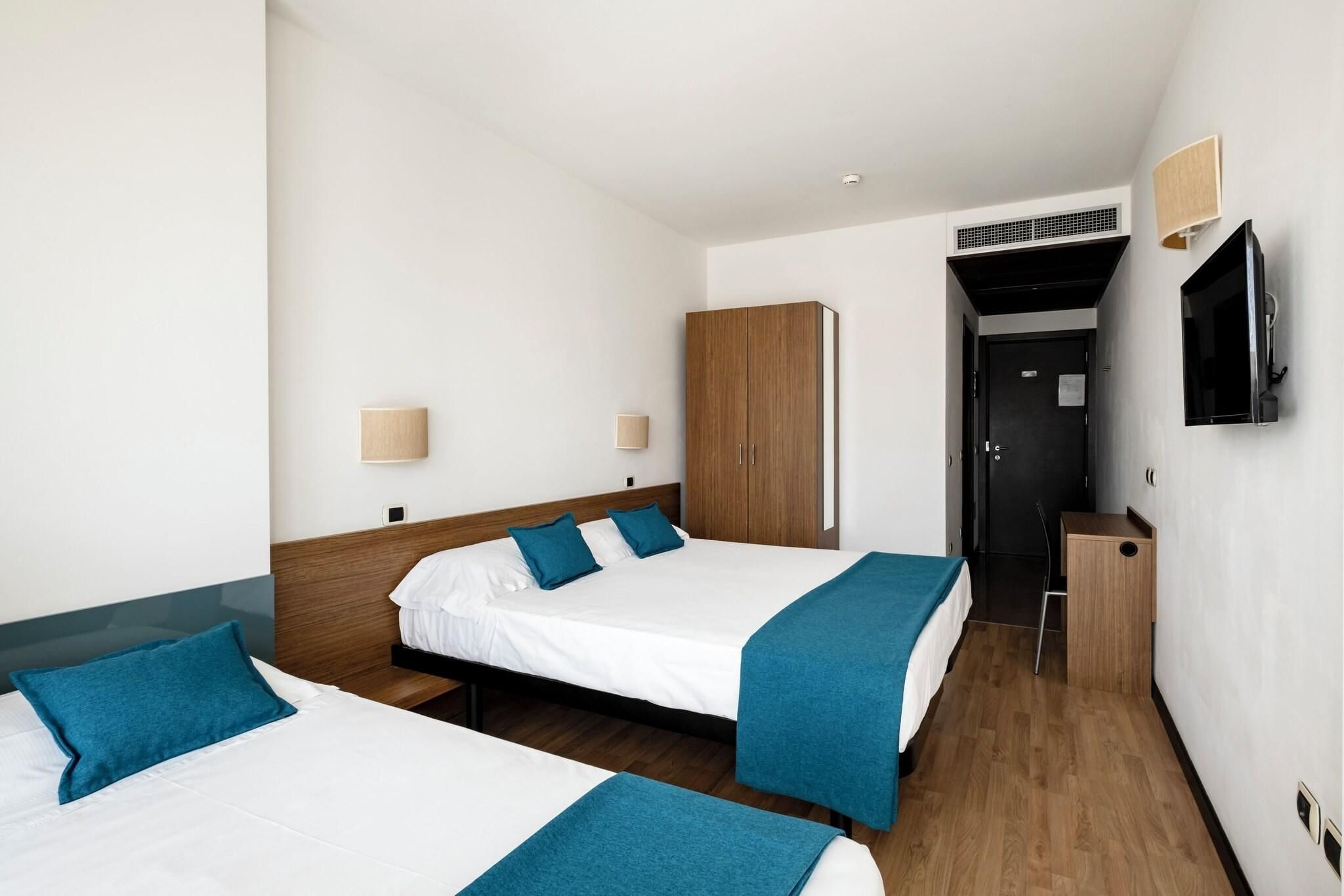 A hotel room with two beds, a wardrobe, a television, and an air conditioning unit.