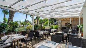 An outdoor restaurant with tables and chairs, a covered area, and potted plants. - Cristallo Rimini (Rimini)