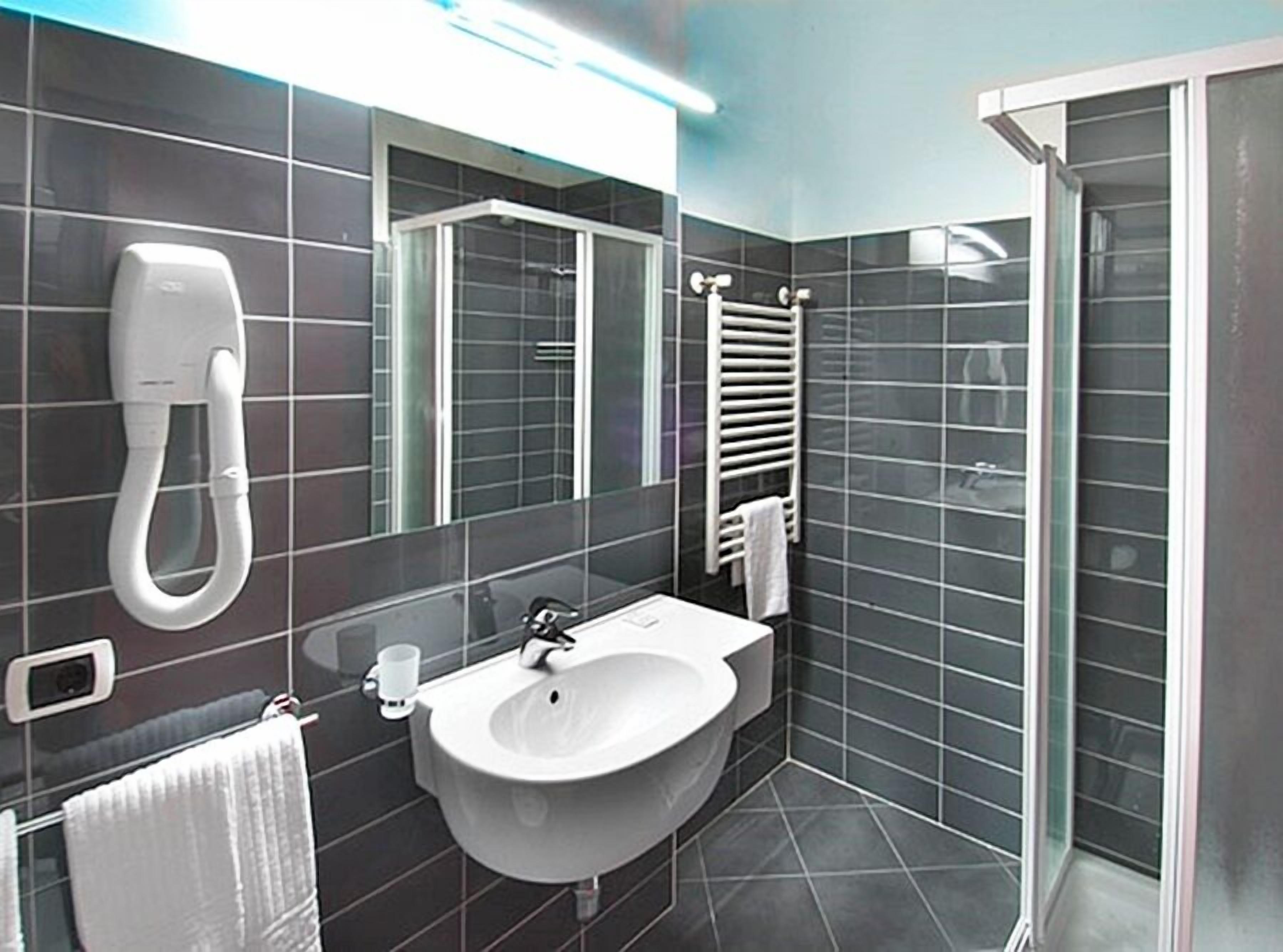 A modern bathroom with a white sink, a mirror, a towel rack, and a glass shower enclosure.