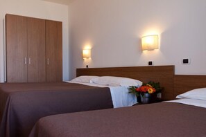 A hotel room with two beds, wooden wardrobe, wall-mounted lights, and a small table with a flower arrangement. - Cristallo Rimini (Rimini)