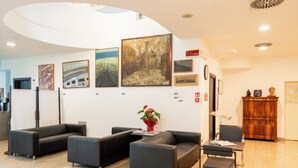 A modern lobby with black leather sofas, a wooden reception desk, and various framed artworks on the walls.