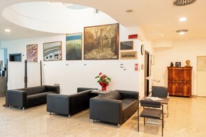 A modern lobby with black leather sofas, a wooden reception desk, and various framed artworks on the walls. - Cristallo Rimini (Rimini)