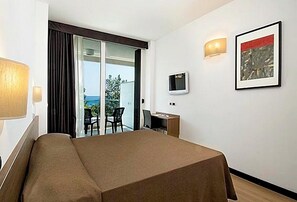 A hotel room with a bed, a desk, a chair, a TV, and a balcony with a view. - Cristallo Rimini (Rimini)