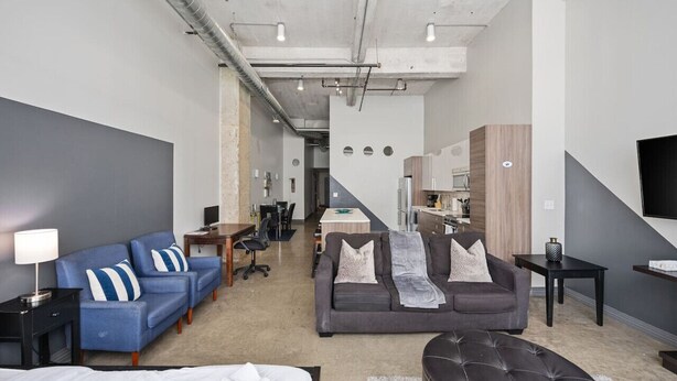 A modern hotel room with a bed, two sofas, a dining area, and a kitchen. - Modern Dallas Retreat with Pool & In-Unit Laundry (Dallas)