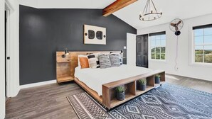A modern bedroom with a large bed, dark walls, and a view of the outdoors through large windows. - Relaxation+Pool & Hot Tub+Views (Comfort)