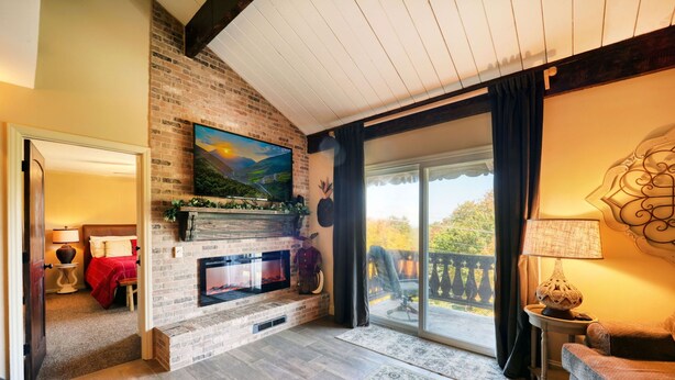 A cozy living room with a fireplace, a large window, and a balcony. - Mountain Getaway Retreat - 4br + loft  (Beech Mountain)