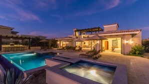 Un área de piscina exterior lujosa, con diversas opciones de asientos y un patio bien iluminado.