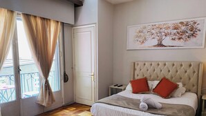 A bedroom with a large bed, a nightstand, a door, and a window with curtains. - BB Casita Blue (Santiago)
