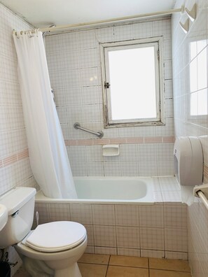 Un baño con inodoro, bañera, ventana y barra de apoyo.