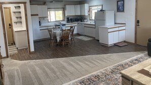 Een kleine keuken met witte kastjes, een eettafel met stoelen, een koelkast en een magnetron.