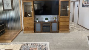 Een woonkamer met een grote flatscreen televisie, houten kasten en een vloerkleed met een patroon.