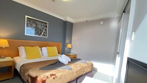 A hotel room with a large bed, two bedside tables, a nightstand, a framed picture on the wall, and a window with a view. - PrimeCozy & Bright 1BR Apartment (Brisbane City)