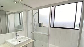 A modern bathroom with a glass-enclosed shower, a white sink, and a large mirror. - PrimeCozy & Bright 1BR Apartment (Brisbane City)