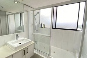 Ein modernes Badezimmer mit einer gläsernen Duschkabine, einem weißen Waschbecken und einem großen Spiegel.