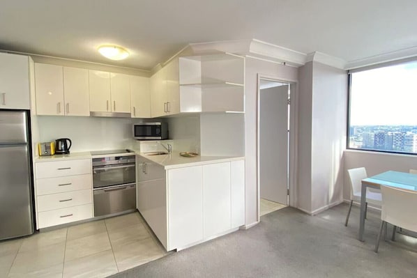 A modern kitchen with white cabinets, stainless steel appliances, and a view of the city through a large window.