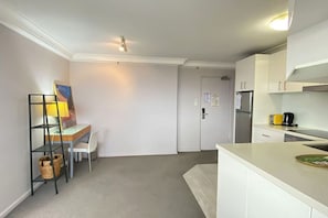Una cocina compacta con gabinetes blancos, un pequeño comedor con una silla y una mesa, y un refrigerador.