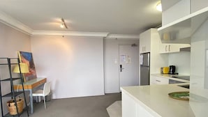 Une cuisine compacte avec des meubles blancs, un petit coin repas avec une chaise et un tableau accroché au mur.