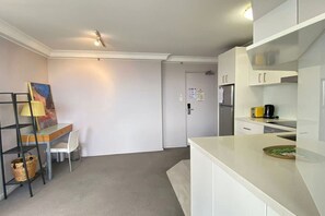 A compact kitchen with white cabinets, a small dining area with a chair, and a painting on the wall.